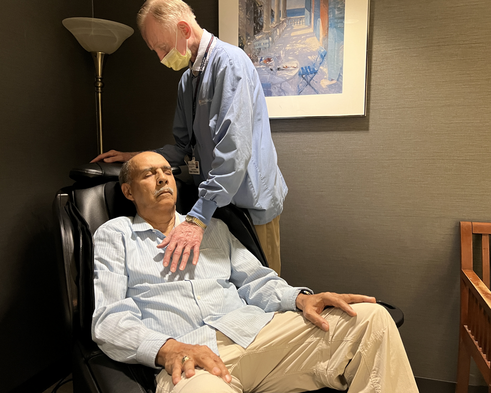 Volunteer Reiki practitioner Vince Gilhool hovers his hand over the chest of a patient seated in a recliner.